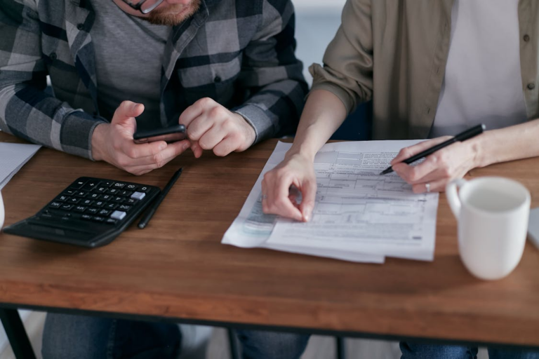 A couple reviewing tax documents at a kitchen table with a calculator