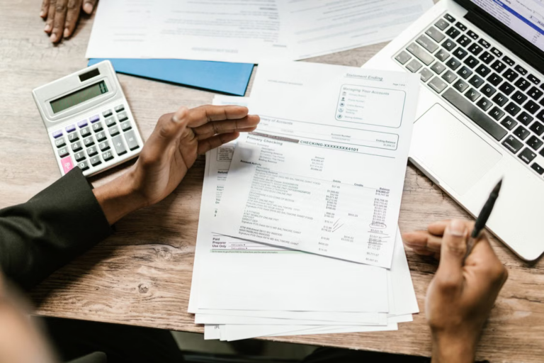 Small business owner reviewing financial reports with a calculator and laptop